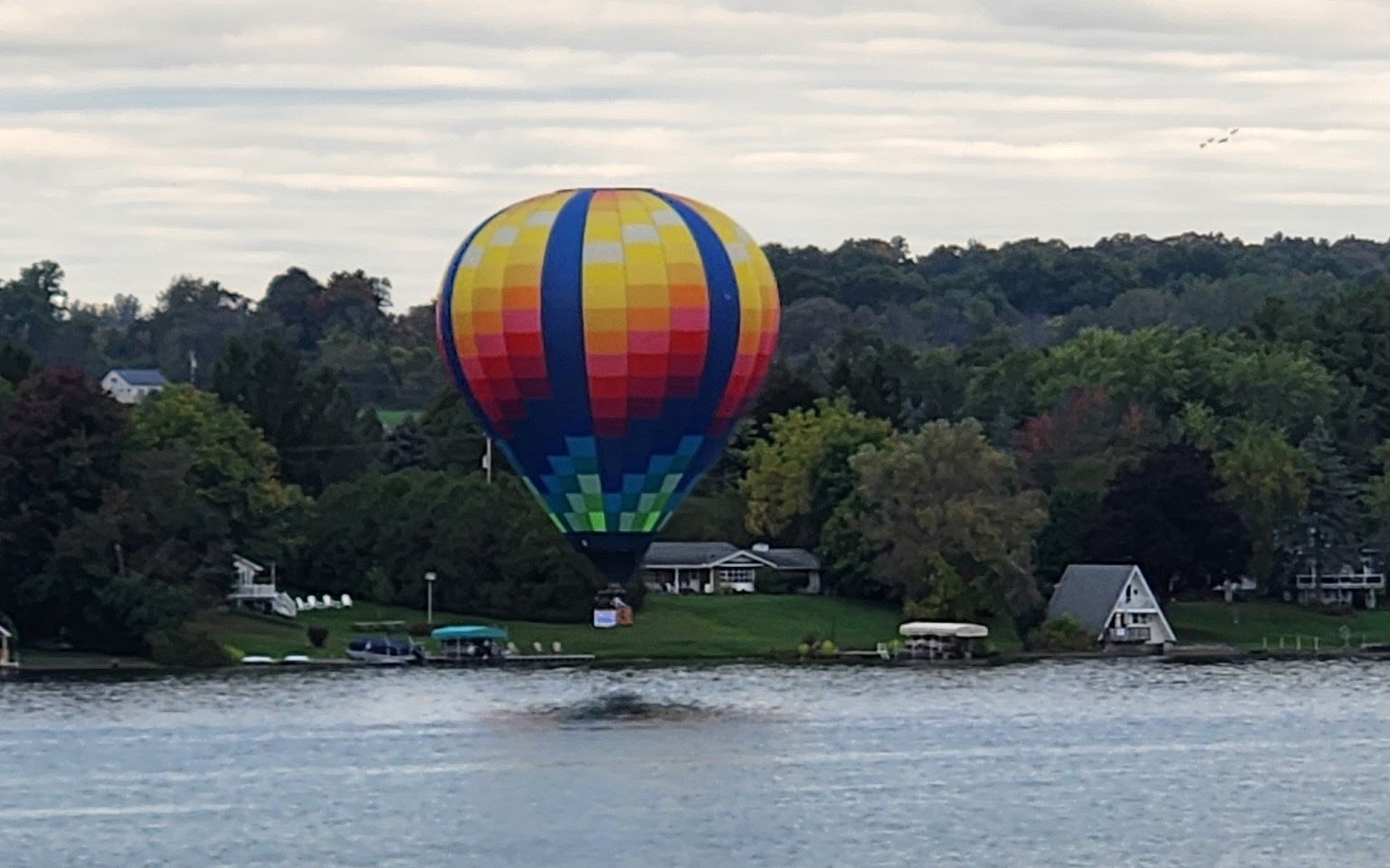 A colorful hot air balloon drifting low over homes and docks along the Silver Lake shoreline